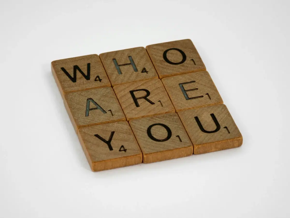Wooden Scrabble tiles spelling out "WHAT ARE YOU" on a white background.