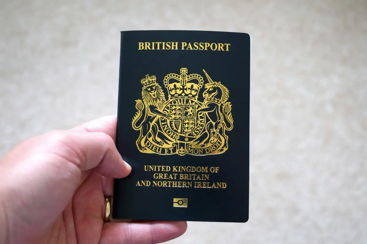 A British passport with a black cover and gold emblem, held in a person's hand against a neutral background.