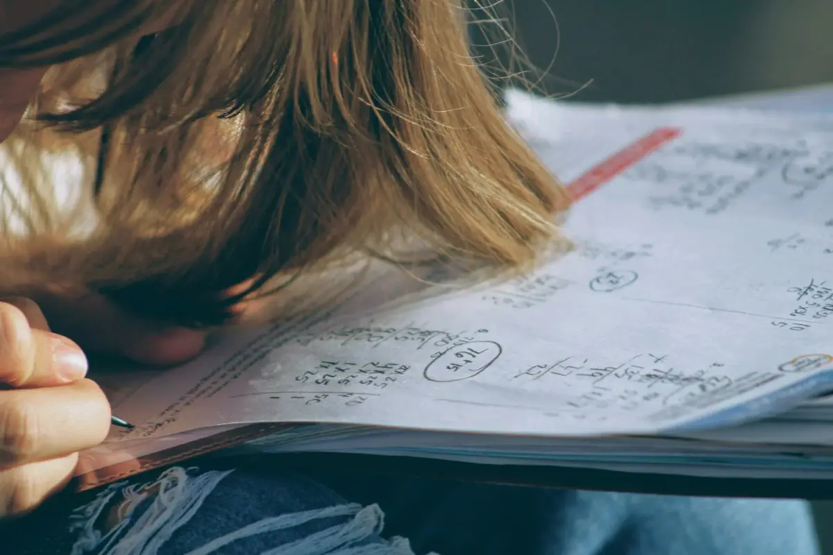 A person with long hair is writing notes in a notebook with handwritten formulas and calculations.