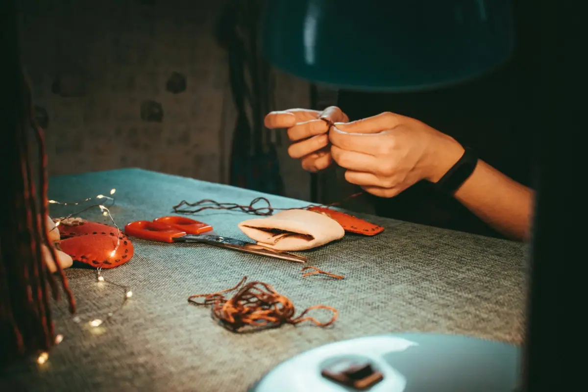 Person sewing leather pieces together with scissors, fabric, and sewing tools on the table.