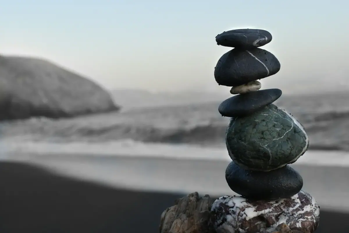 Stacked smooth stones on a beach with ocean waves and distant land in the background, in a muted color palette.