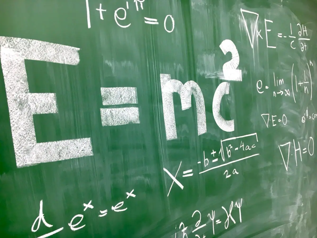 A green chalkboard filled with various mathematical and physics equations written in white chalk, including the formula for Einstein's energy-mass equivalence, quantum mechanics equations, and calculus.