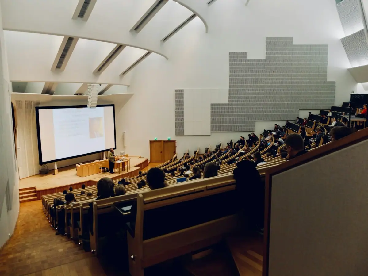 University lecture hall filled with students listening to a presentation at the front.