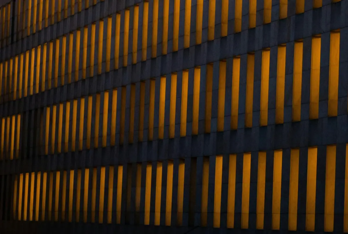 Close-up view of a modern building facade with vertical yellow-lit panels on a dark background.