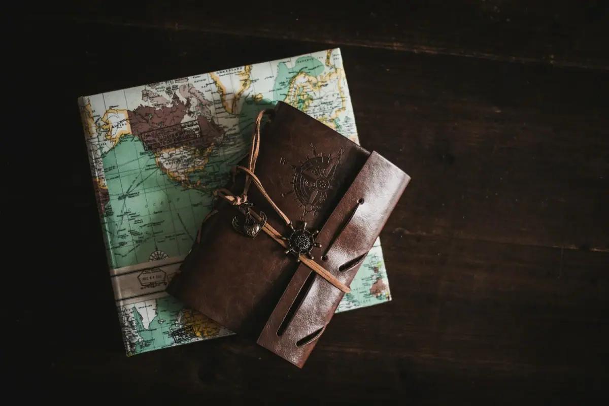 Travel-themed items including a world map, a leather journal, and a vintage-style compass on a dark wooden surface.