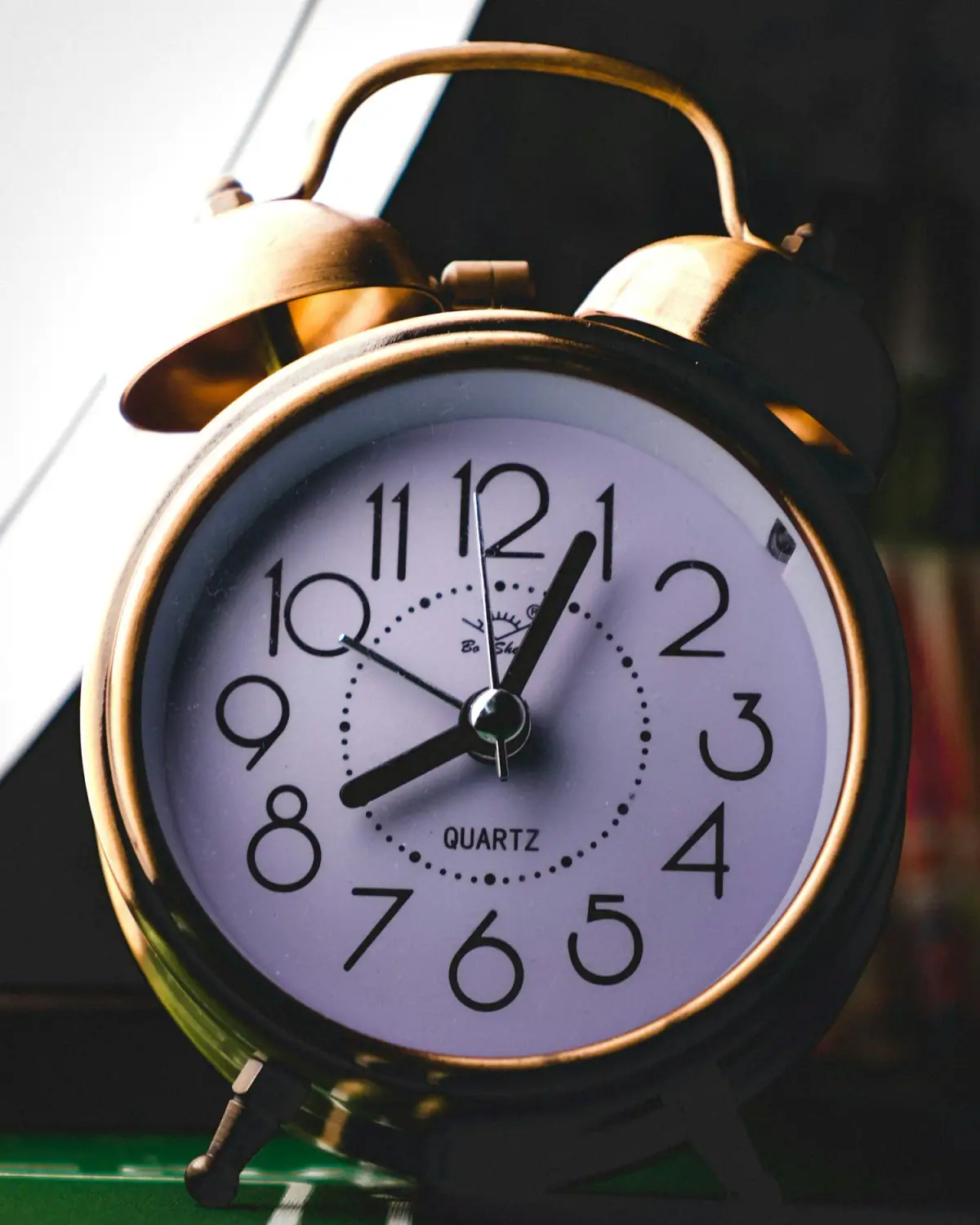 A vintage-style alarm clock showing the time as 8:02, with a white face and black numbers, a brass-colored frame, and two bells on top.